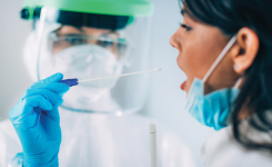 Female clinician wearing PPE swabs a young womans mouth